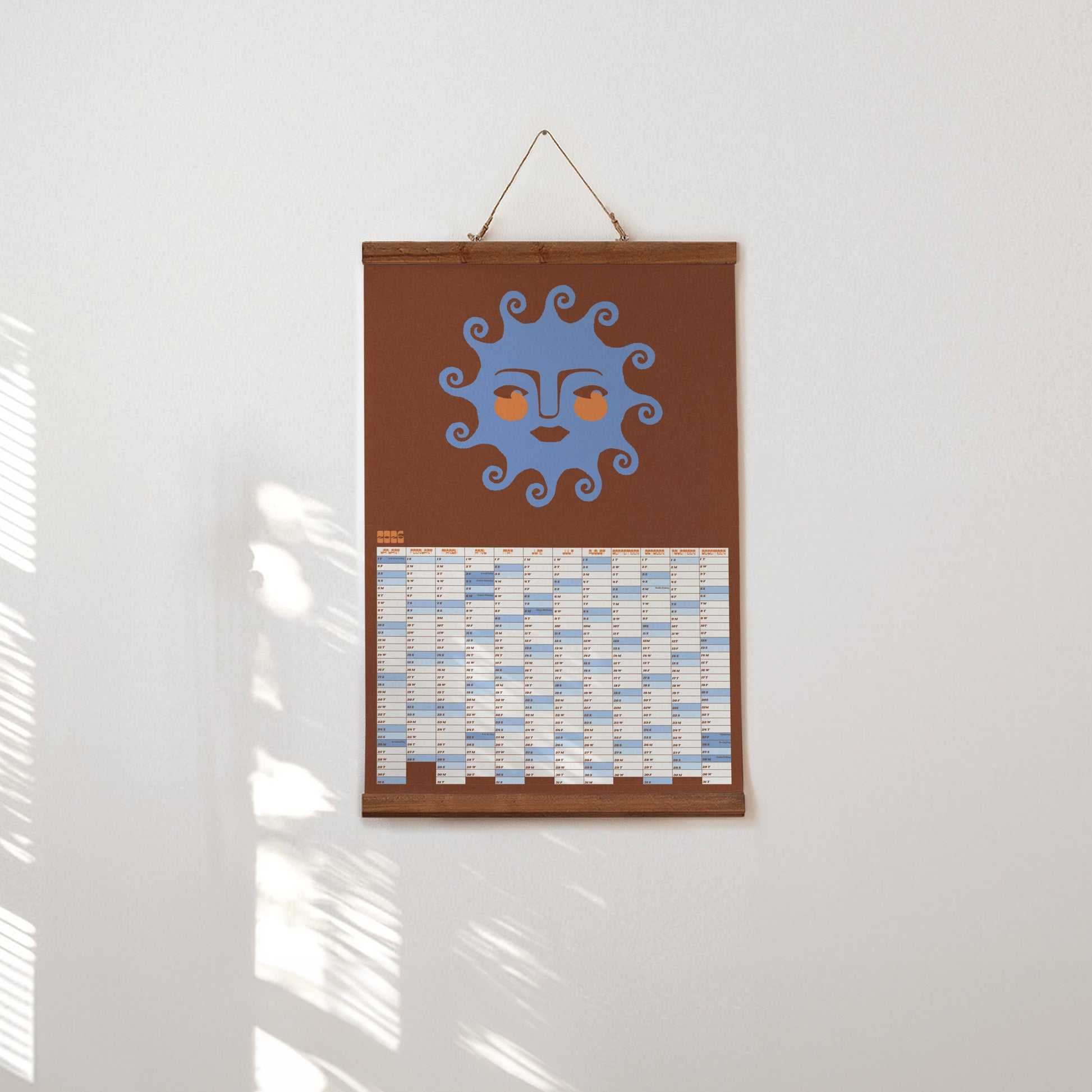 Decorative wall hanging with a sun design on a brown background, hanging on a white wall.