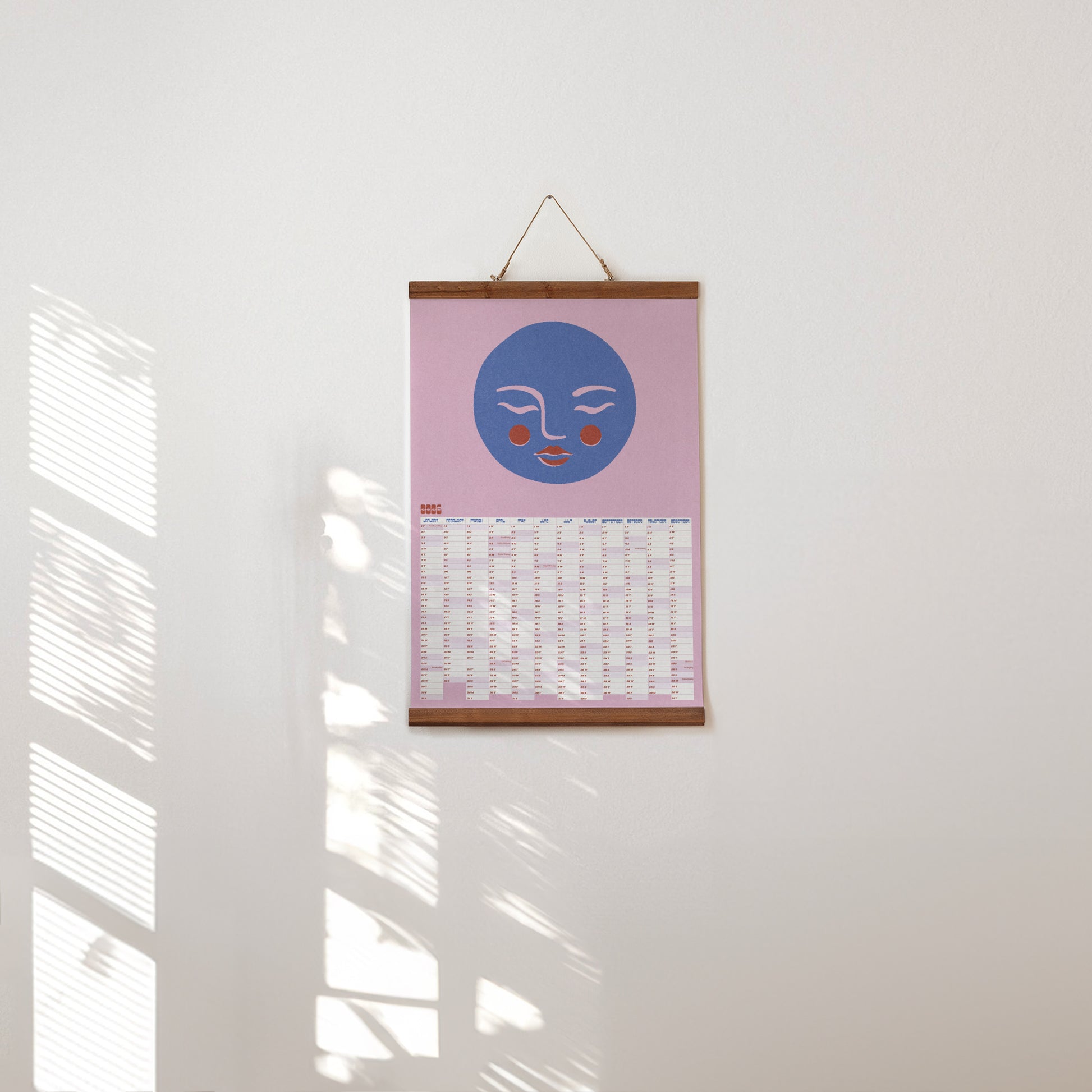 Poster with a blue Moon face design on a pink background hanging on a white wall.