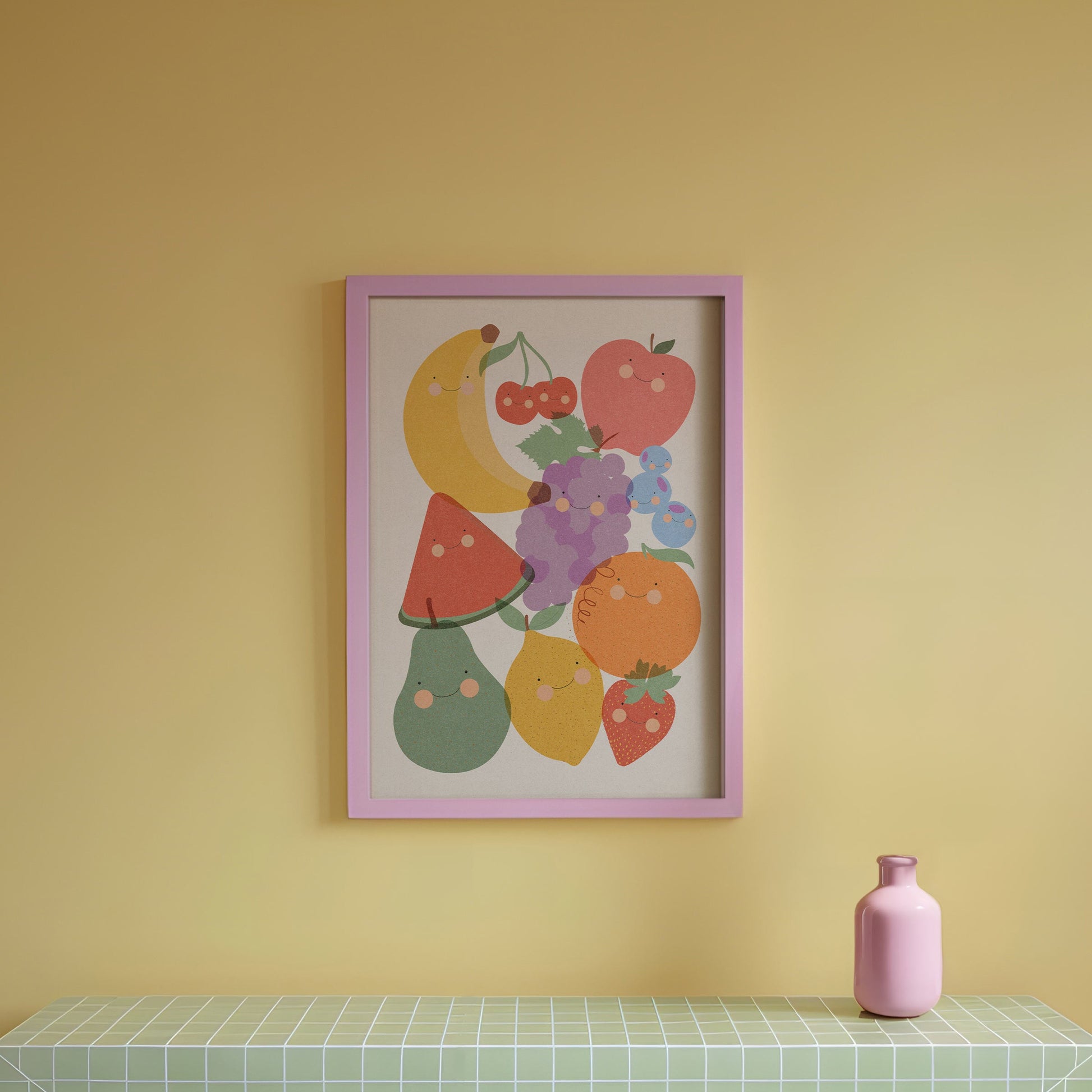 Green tiled table with a pink vase against a yellow wall with a colorful fruit print.
