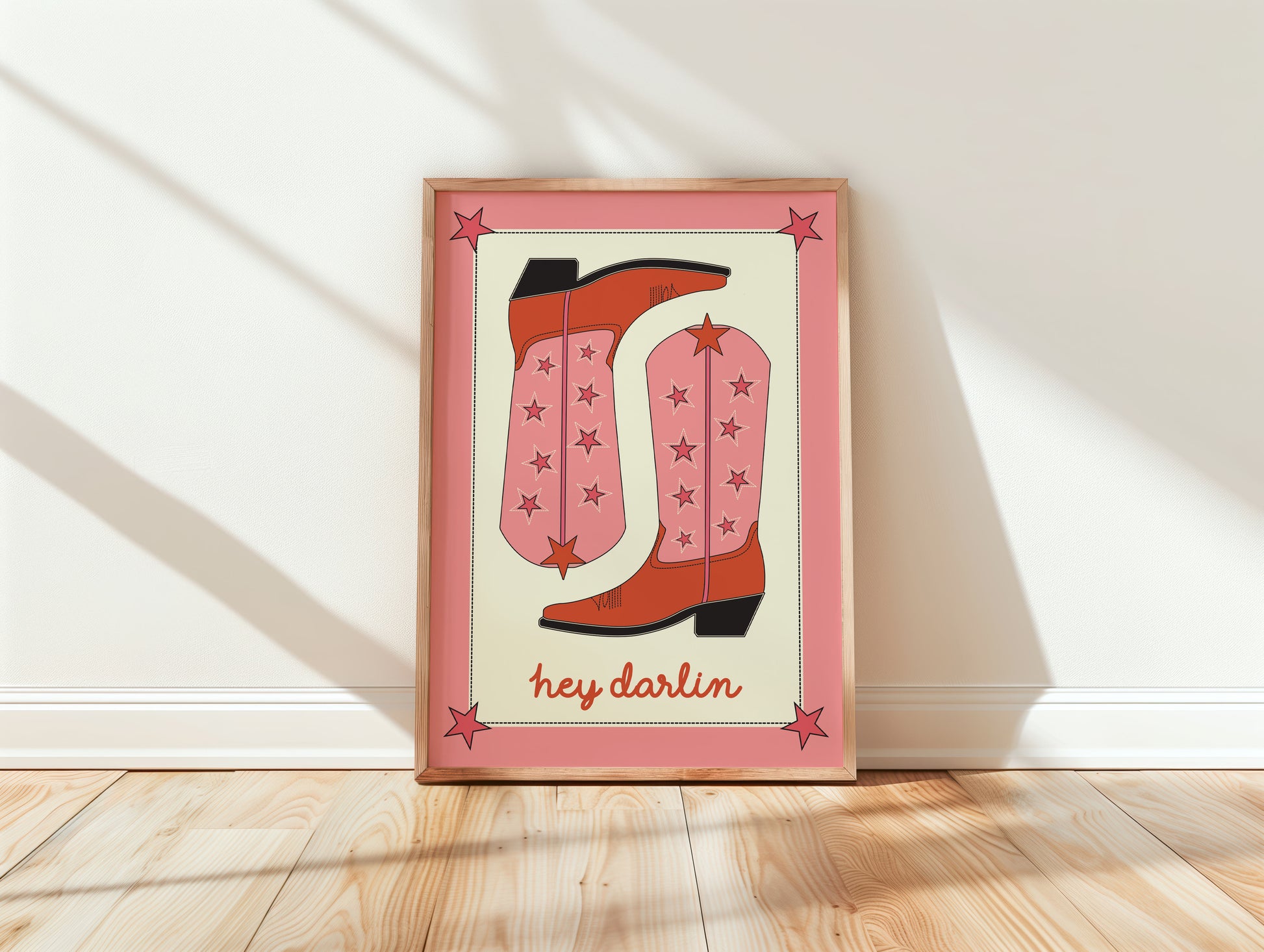 Framed artwork with pink cowboy boots and 'hey darlin' text on a white wall.