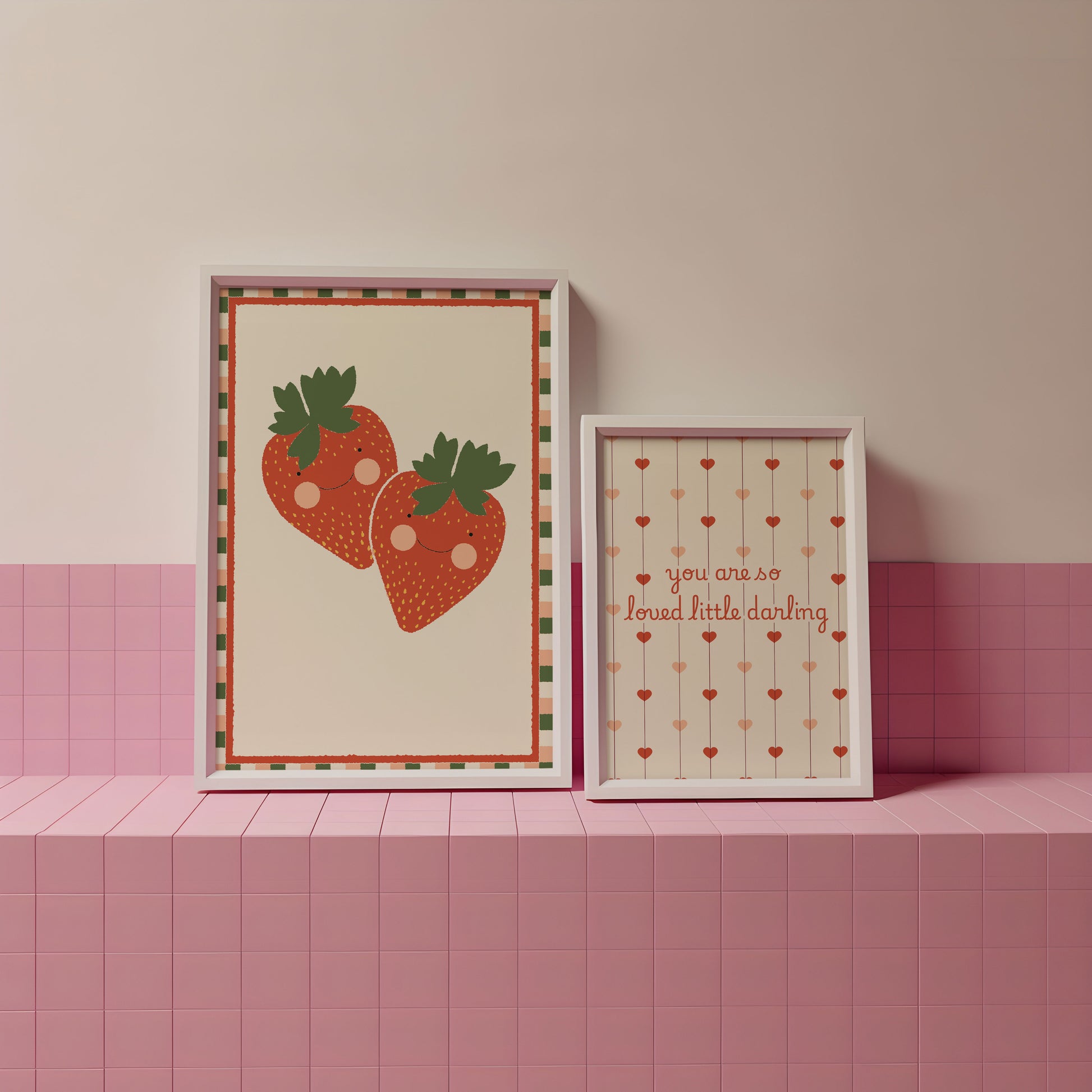 Two framed prints on a pink tiled surface with a neutral wall background