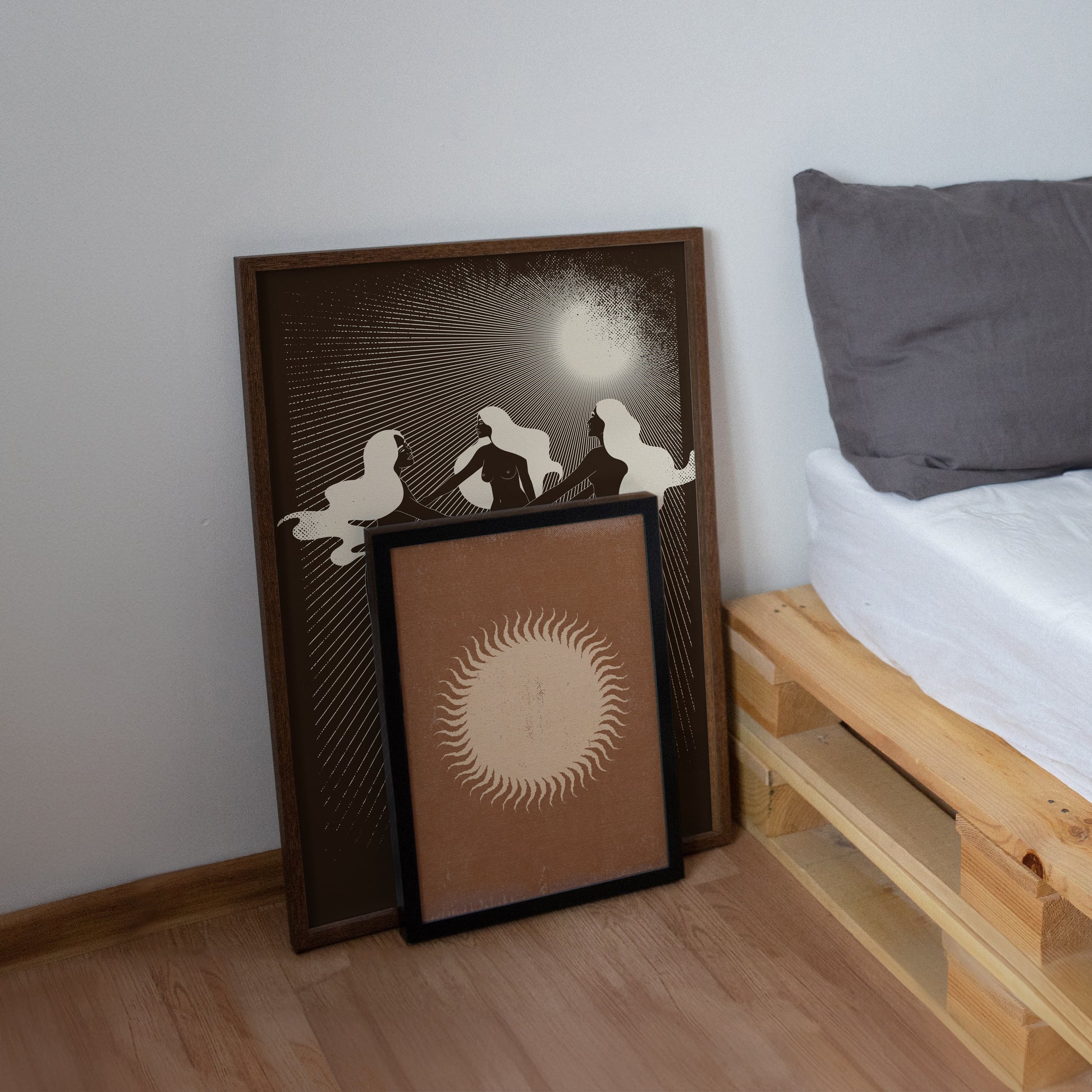 Two framed artworks leaning against a wall next to a bed with wooden headboard.